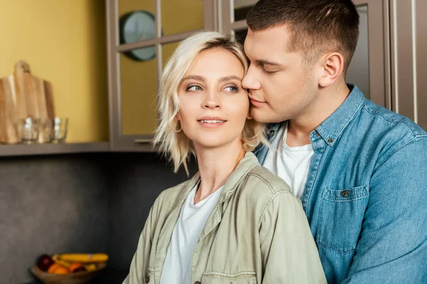 Sorridente giovane coppia amorevole che abbraccia in cucina a casa — Foto stock