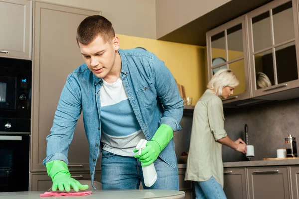 Selective focus of man cleaning table near woman in kitchen at home — Stock Photo