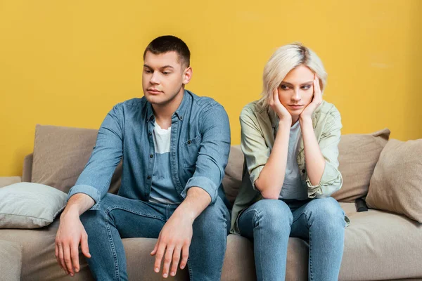 Triste jeune couple assis sur le canapé près du mur jaune — Photo de stock