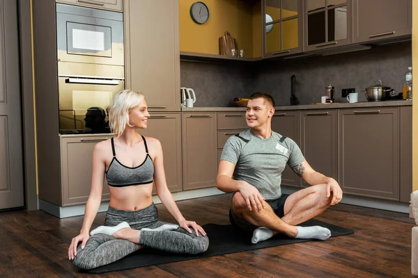 Sonriente joven pareja practicando yoga juntos en pose de loto en casa durante la cuarentena - foto de stock