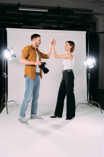 Vue latérale du modèle souriant high five chez le photographe avec appareil photo numérique en studio photo — Photo de stock