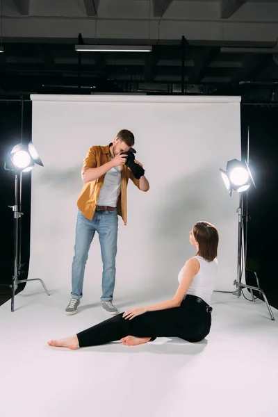 Fotógrafo usando câmera digital enquanto trabalha com modelo em estúdio de fotografia — Fotografia de Stock