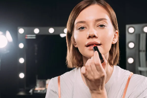 Attraktive Frau blickt in die Kamera, während sie im Fotostudio roten Lippenstift aufträgt — Stockfoto