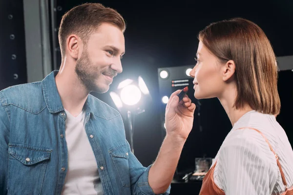 Handsome makeup artist smiling while applying lipstick on attractive model — Stock Photo