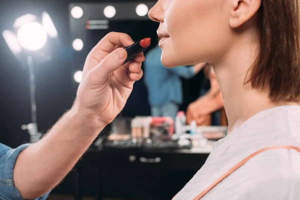 Обрезанный вид визажиста, держащего красную помаду возле молодой модели в фотостудии — стоковое фото