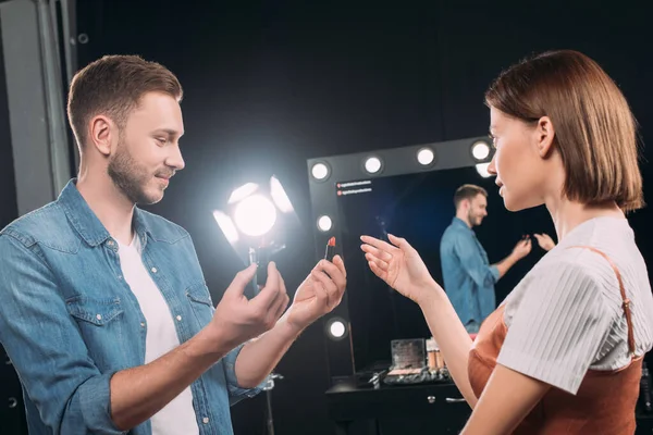 Makeup artist holding lipsticks near young model in photo studio — Stock Photo