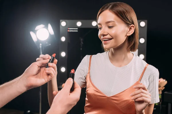 Modello sorridente che prende il rossetto dall'artista del trucco in studio fotografico — Foto stock