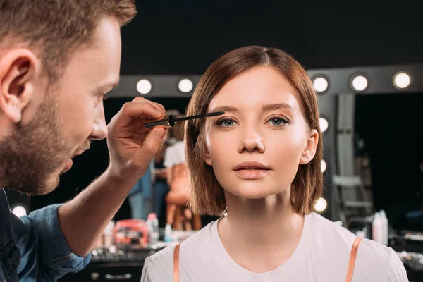 Selective focus of makeup artist applying mascara on young model in photo studio — Stock Photo
