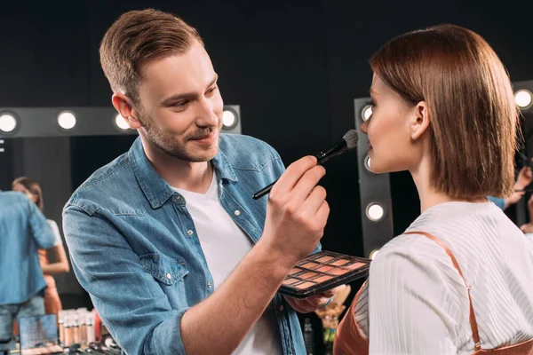 Artista de maquiagem sorridente aplicando blush em modelo jovem no estúdio de fotos — Fotografia de Stock