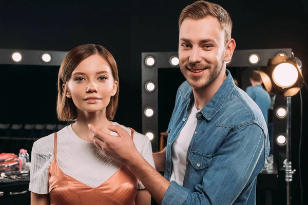 Bellissimo truccatore sorridente alla fotocamera vicino a un bellissimo modello in studio fotografico — Foto stock