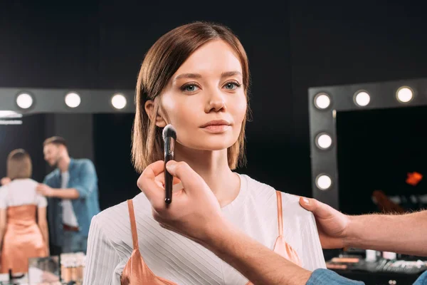 Maquillaje artista aplicación de polvo facial en hermosa modelo - foto de stock