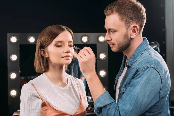 Handsome makeup artist applying eye shadow on model in photo studio — Stock Photo
