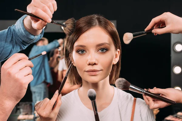 Makeup artists holding cosmetic brushes near beautiful model in photo studio — Stock Photo