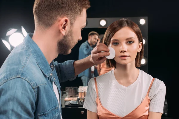 Maquillaje artista sosteniendo almohadilla de algodón cerca de la cara de la hermosa mujer en estudio de fotos — Stock Photo