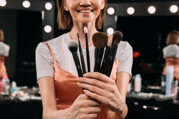 Foco seletivo de mulher sorridente segurando escovas cosméticas no estúdio de fotos — Fotografia de Stock