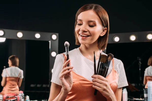 Modelo positivo que sostiene cepillos cosméticos cerca de espejos en el fondo en el estudio de fotos — Stock Photo