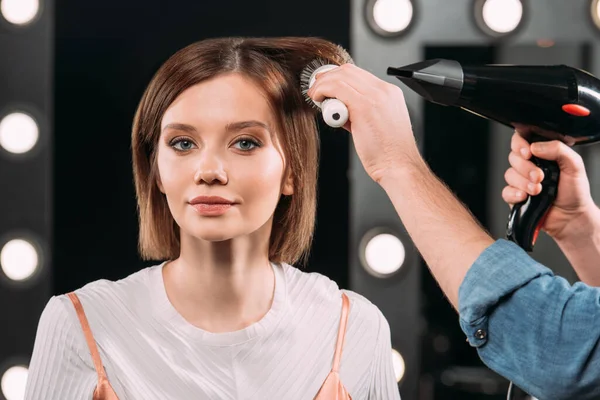 Maquillaje artista haciendo peinado con cepillo de pelo y secador de pelo a la mujer atractiva — Stock Photo