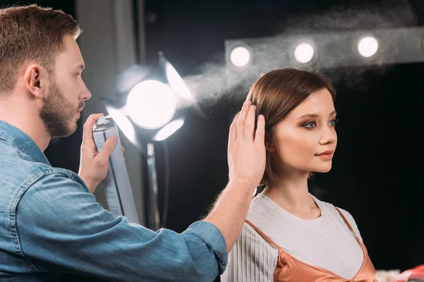 Handsome makeup artist using hair spray while doing hairstyle to beautiful model in photo studio — Stock Photo