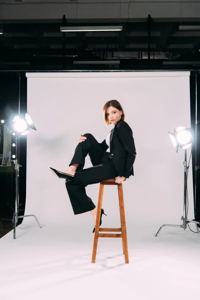 Vue latérale du modèle à la mode posant sur une chaise dans un studio photo — Photo de stock