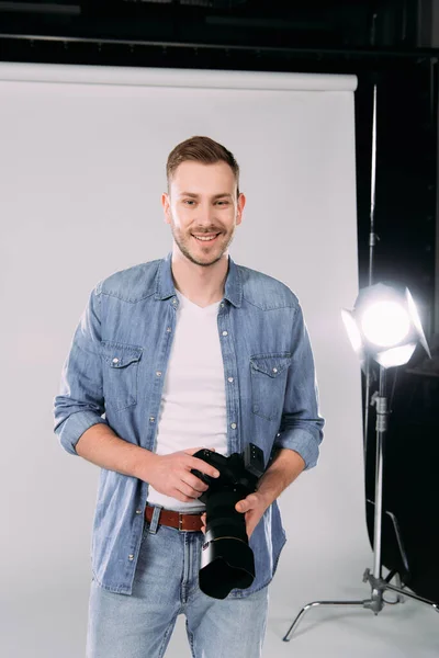 Fotógrafo sosteniendo cámara digital y sonriendo en estudio fotográfico - foto de stock