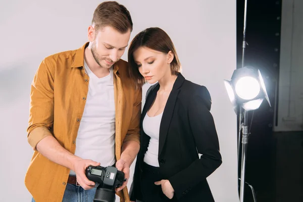 Handsome photographer and elegant model looking at display of digital camera in photo studio — Stock Photo