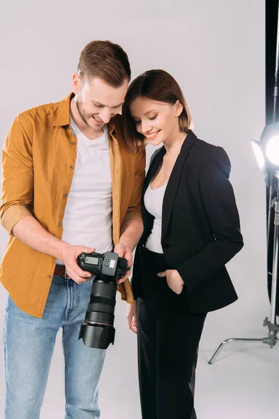 Handsome photographer and beautiful smiling woman looking at display of digital camera in photo studio — Stock Photo