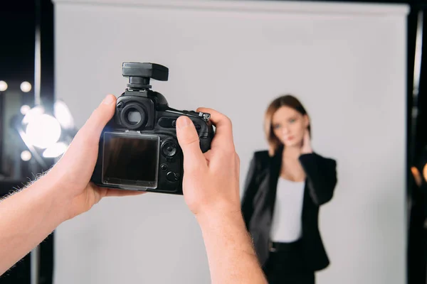 Enfoque selectivo del fotógrafo que sostiene la cámara digital cerca del modelo en el estudio fotográfico - foto de stock