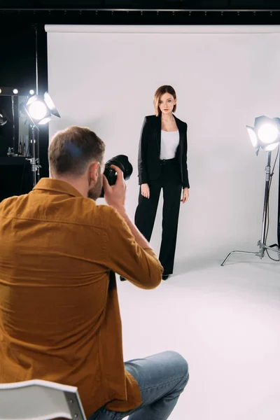 Focus sélectif du photographe avec appareil photo numérique travaillant avec un modèle élégant en studio photo — Photo de stock