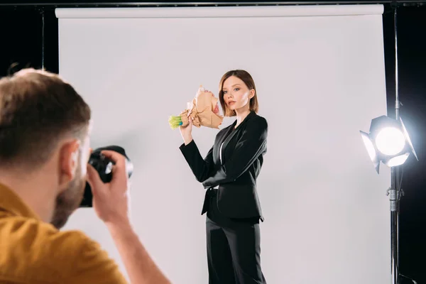 El foco selectivo del fotógrafo tomando la foto del modelo elegante con el ramo en el estudio fotográfico - foto de stock