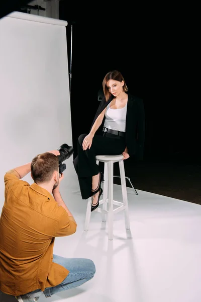 Fotografo che lavora con bella modella in posa sulla sedia in studio fotografico — Foto stock