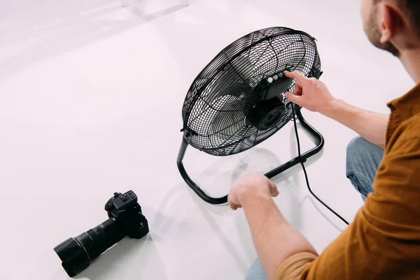 Vue recadrée du photographe ajustant le ventilateur électrique près de l'appareil photo numérique dans le studio photo — Photo de stock