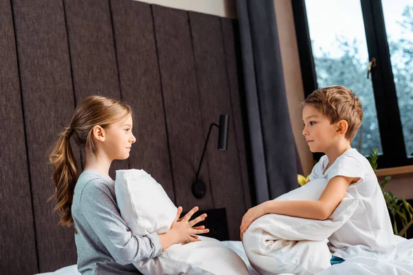 Side view of sister holding pillow and looking at brother in bedroom — Stock Photo