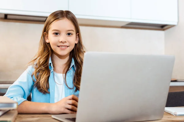 Enfoque selectivo de niño feliz en línea estudiando cerca de la computadora portátil en casa - foto de stock