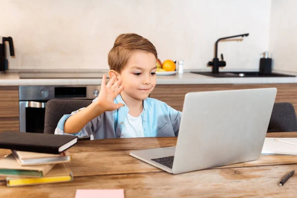 Messa a fuoco selettiva del bambino carino agitando la mano e guardando il computer portatile mentre e-learning a casa — Foto stock