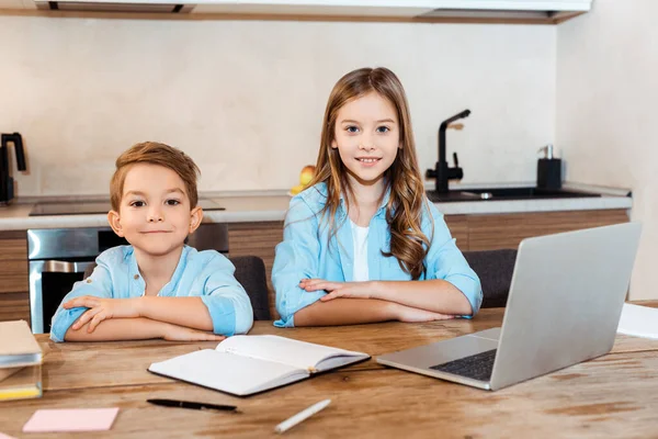 Selective focus of happy sister and brother sitting near laptop while e-learning at home — Stock Photo