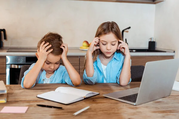 Hermanos cansados e-learning cerca de portátil y portátil en casa - foto de stock