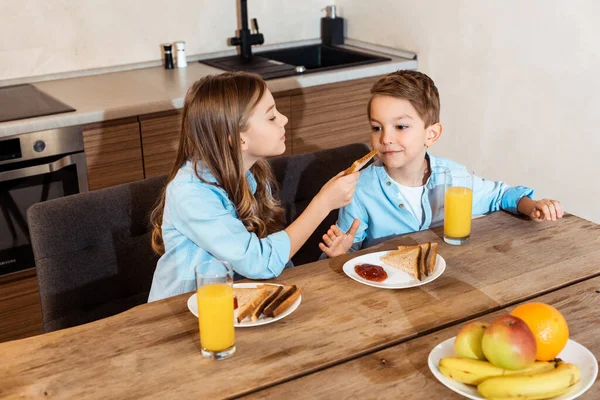 Cute sister feeding brother with toast bread at home — Stock Photo