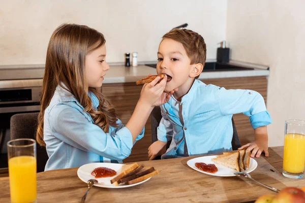 Foco seletivo de irmã feliz alimentando irmão bonito com pão saboroso torrada em casa — Fotografia de Stock