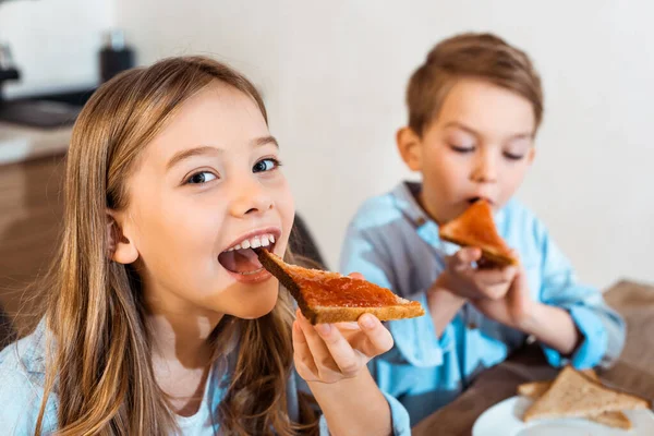 Selective focus of cheerful siblings eating toast bread with bread — Stock Photo
