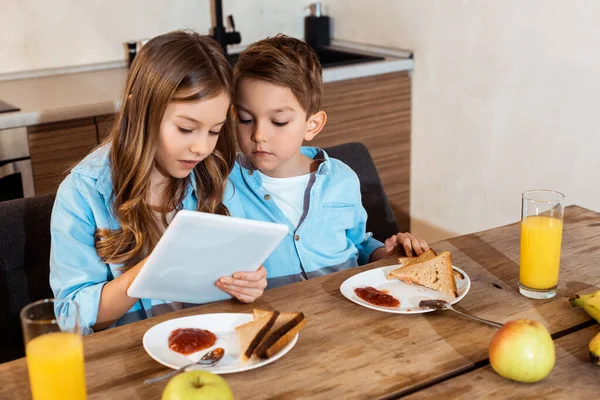 Брати і сестри дивляться на цифровий планшет біля смачного сніданку — стокове фото