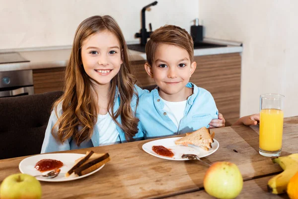 Enfoque selectivo de los hermanos felices sonriendo cerca de sabroso desayuno - foto de stock