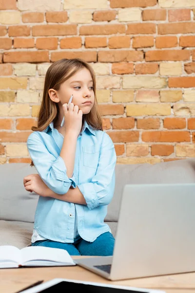 Concentrazione selettiva del bambino pensieroso che tiene la penna e distoglie lo sguardo mentre e-learning a casa — Foto stock