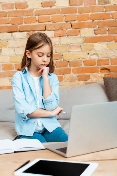 Selective focus of sad kid holding pen while e-learning at home — Stock Photo