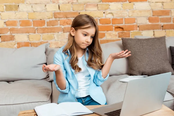 Confused kid showing shrug gesture and looking at laptop — Stock Photo
