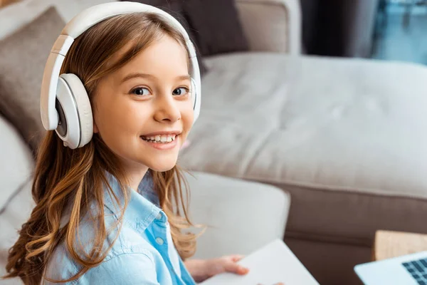 Glückliches Kind mit drahtlosen Kopfhörern, das in die Kamera schaut — Stockfoto