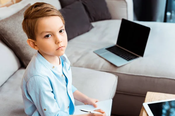 Tired boy looking at camera near gadgets with blank screen — Stock Photo