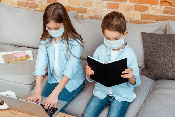 Hermanos en máscaras médicas e-learning en sala de estar - foto de stock