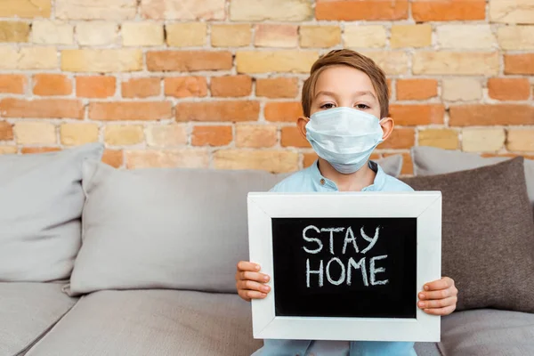 Menino em máscara médica segurando quadro com ficar em casa lettering — Fotografia de Stock