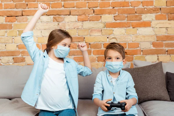 KYIV, UKRAINE - APRIL 27, 2020: sister gesturing near brother in medical mask playing video game — Stock Photo