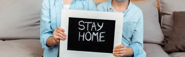 Tiro panorâmico de irmãos segurando quadro com ficar em casa lettering — Fotografia de Stock